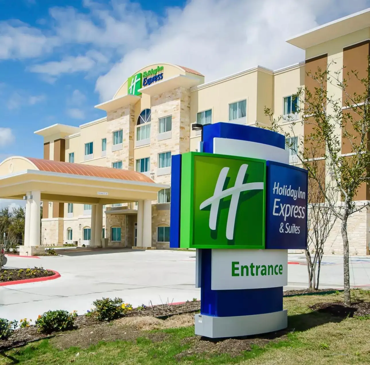 A Holiday Inn Express & Suites in cream stucco and limestone, its entrance sign in the foreground