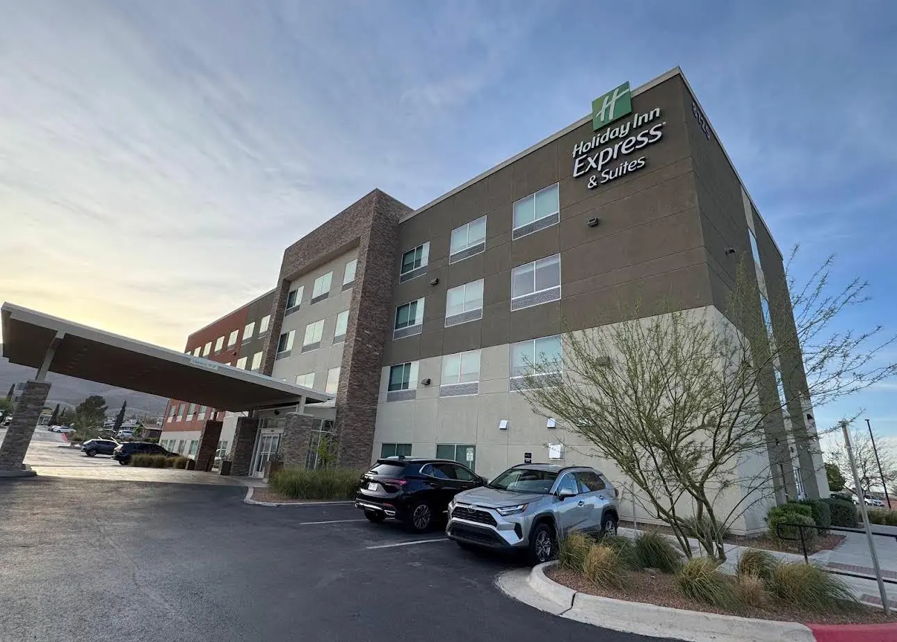 A Holiday Inn Express & Suites in dark stucco and stone at dusk, the entrance canopy at the left and hills behind