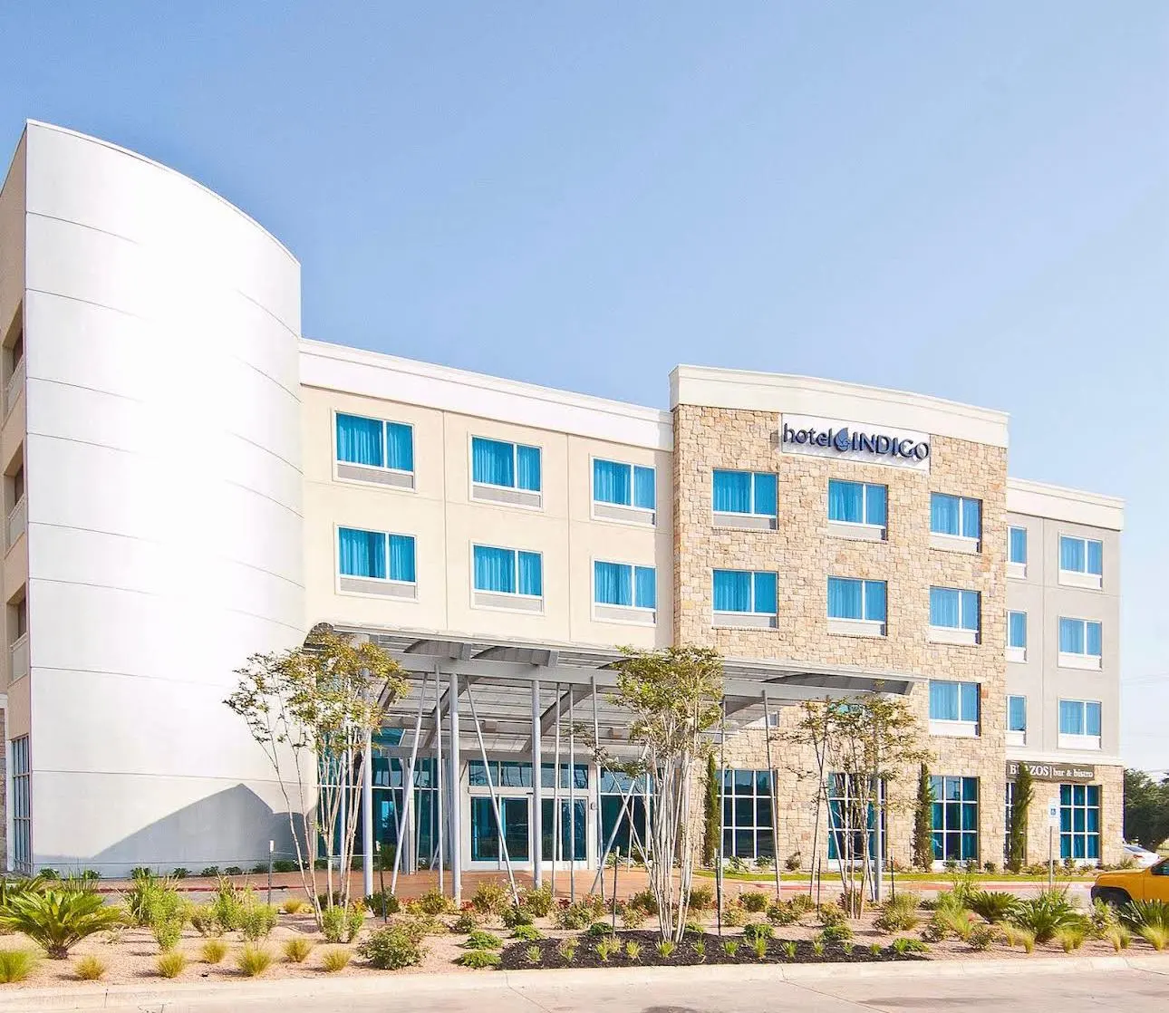 A Hotel Indigo in cream stucco and limestone under a clear sky, a steel canopy over the entrance